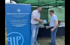 Zdjęcie przy stoisku Okręgu. Inspektor pracy wręcza broszurę osobie odwiedzającej stoisko