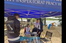 Widok na stoisko OIP. Niebieski namiot wystawienniczy, pod zadaszeniem stolik, ulotki, plakaty oraz osoby obsługujące i zainteresowani 