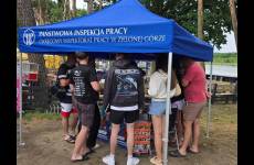 Widok na stoisko OIP. Niebieski namiot wystawienniczy, pod zadaszeniem stolik, ulotki, plakaty oraz osoby obsługujące i zainteresowani 