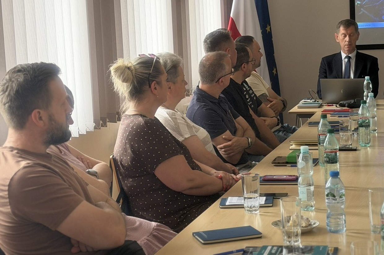 Trwa szkolenie. Uczestnicy szkolenia siedzą przy stołach, przed nimi prelegent prowadzi wykład