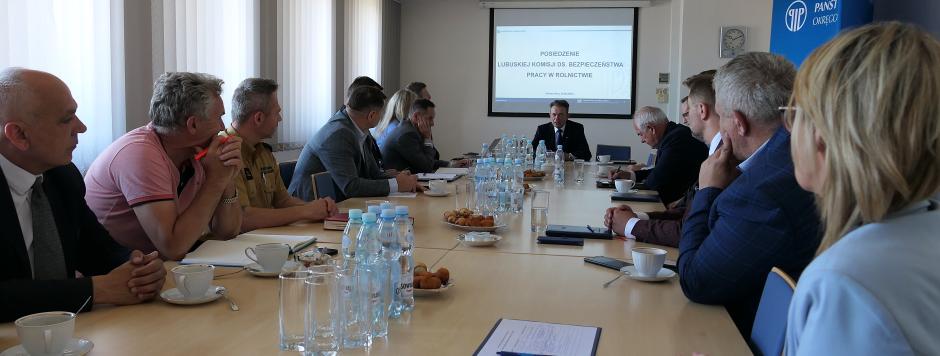 Widok sali konferencyjnej. Przy stołach siedzą uczestnicy spotkania, na ekranie zawieszonym na ścianie wyświetlony jest slajd z prezentacji multimedialnej